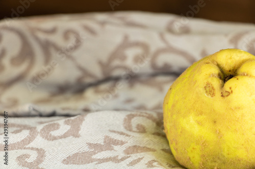 Coing entier jaune à peau duveteuse après une récolte automnale posé sur un torchon gris avec des arabesques fond en bois espace négatif pour texte photo