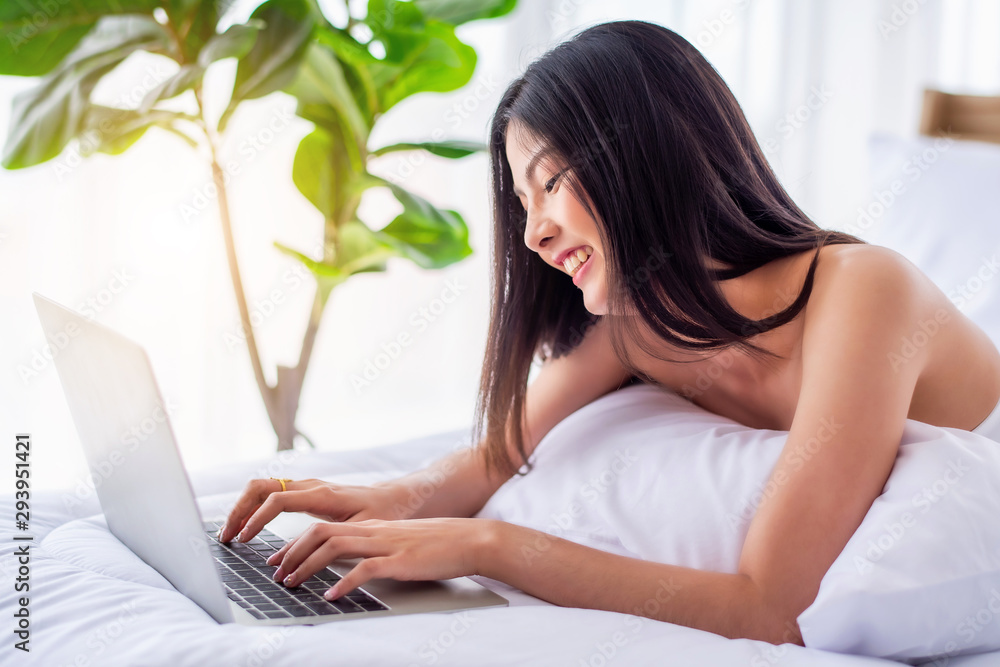 Pretty attractive sensuality young Asian woman wearing red bra and using laptop, laying on the white bed at bedroom in the morning Pretty attractive sensuality young Asian woman wearing red bra and using laptop, laying on the white bed at bedroom in the morning