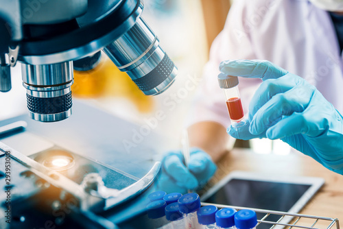 lab technician assistant analyzing a blood sample in test tube at laboratory with microscope. Medical, pharmaceutical and scientific research and development concept. photo