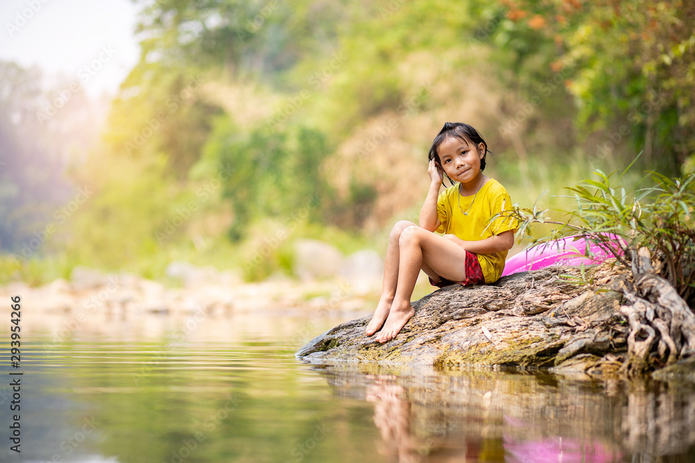 Adorable Asian girl sitting on riverside rock with her pool ring aside Adorable Asian girl sitting on riverside rock with her pool ring aside