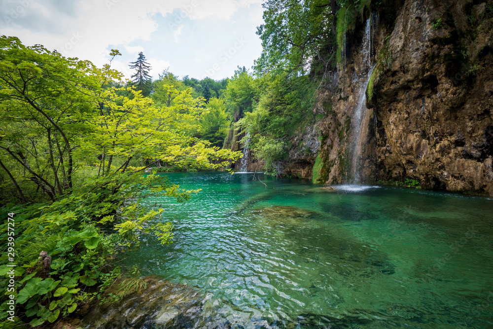 The water of a small creek rushes down the rock face into the azure coloured water of a pond at the Plitvice Lakes National Park in Croatia The water of a small creek rushes down the rock face into the azure coloured water of a pond at the Plitvice Lakes National Park in Croatia