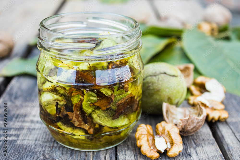 Tincture or elixir with walnuts in a glass jar near the walnut kernel on an old wooden table. Tincture or elixir with walnuts in a glass jar near the walnut kernel on an old wooden table.