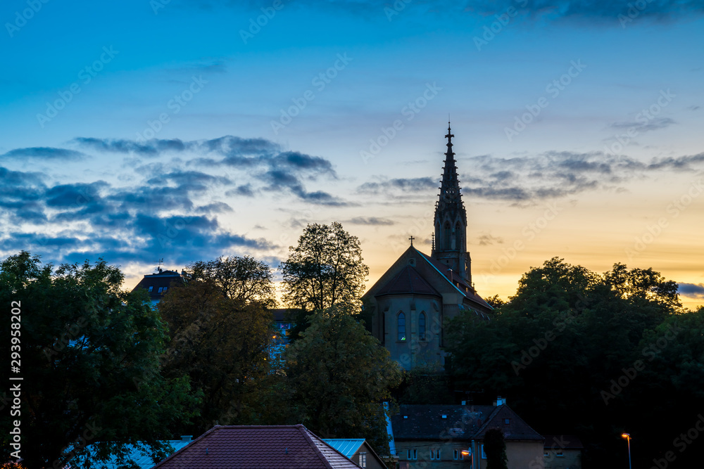 Fototapeta premium Germany, Beautiful sunset sky decorating medieval ancient church and skyline of stuttgart district berg, called berger church surrounded by trees, seen from above the roofs HDR