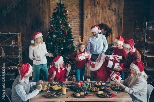 Photo of large family with small little kids senior pensioner sit table on x-mas meal celebration in santa claus cap hat get receive wish gift boxes house having x-mas tree atmosphere spirit