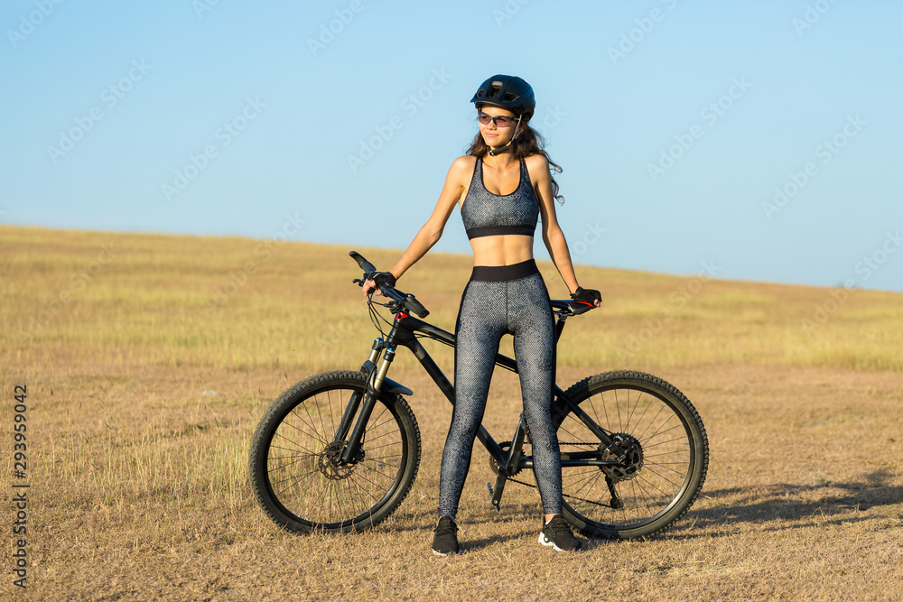Girl on a mountain bike on offroad, beautiful portrait of a cyclist at sunset, Fitness girl rides a modern carbon fiber mountain bike in sportswear, a helmet, glasses and gloves. Girl on a mountain bike on offroad, beautiful portrait of a cyclist at sunset, Fitness girl rides a modern carbon fiber mountain bike in sportswear, a helmet, glasses and gloves.