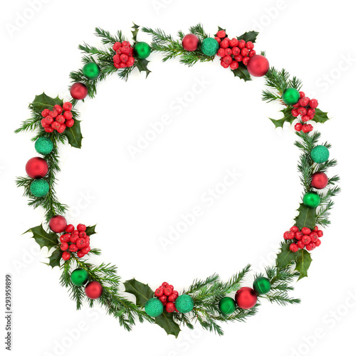 Christmas wreath abstract decoration with winter flora of juniper fir and holly with red and green baubles on white background with copy space. Decorative symbol for the festive season.