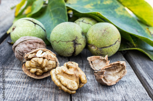Walnut kernels and whole walnuts lie next to nuts in green shells and green leaves on a rustic old wooden table.