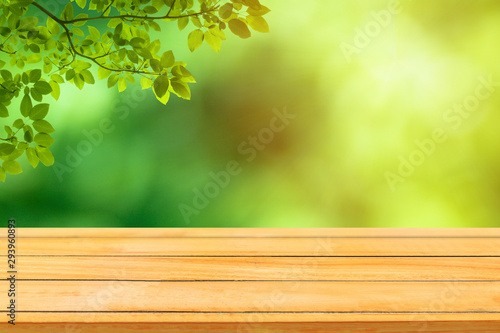 Wooden table with green natural view of green leaves in garden with sunlight in the morning.
