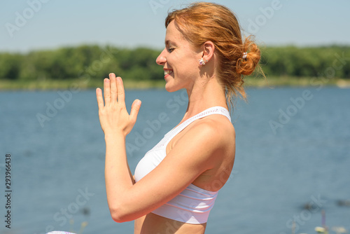 Young girl practices yoga near the river on a clear sunny day