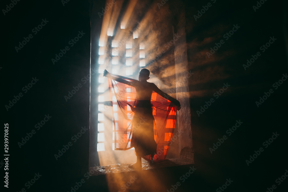 Children monk praying at the buddhist temple. artistic portrait with a monk silhouette in the mist and light filtering from a window - obrazy, fototapety, plakaty 