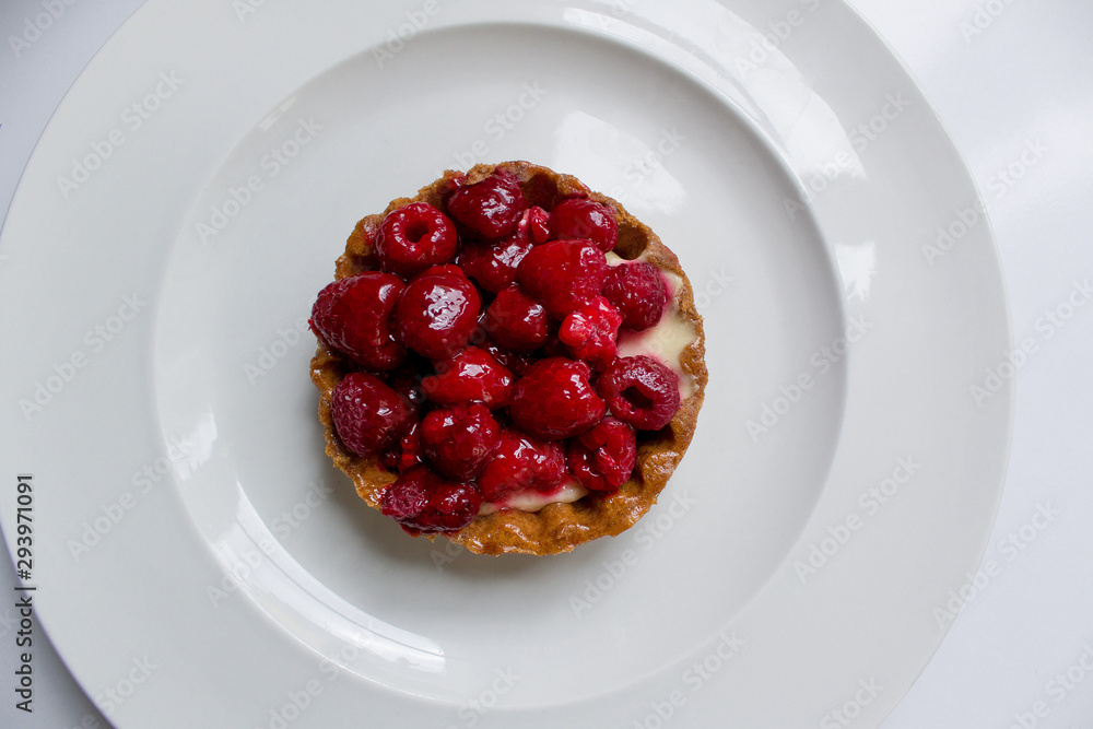top view fresh baked sweet sugar french tartlet of raspberry on circle of white plate background top view fresh baked sweet sugar french tartlet of raspberry on circle of white plate background