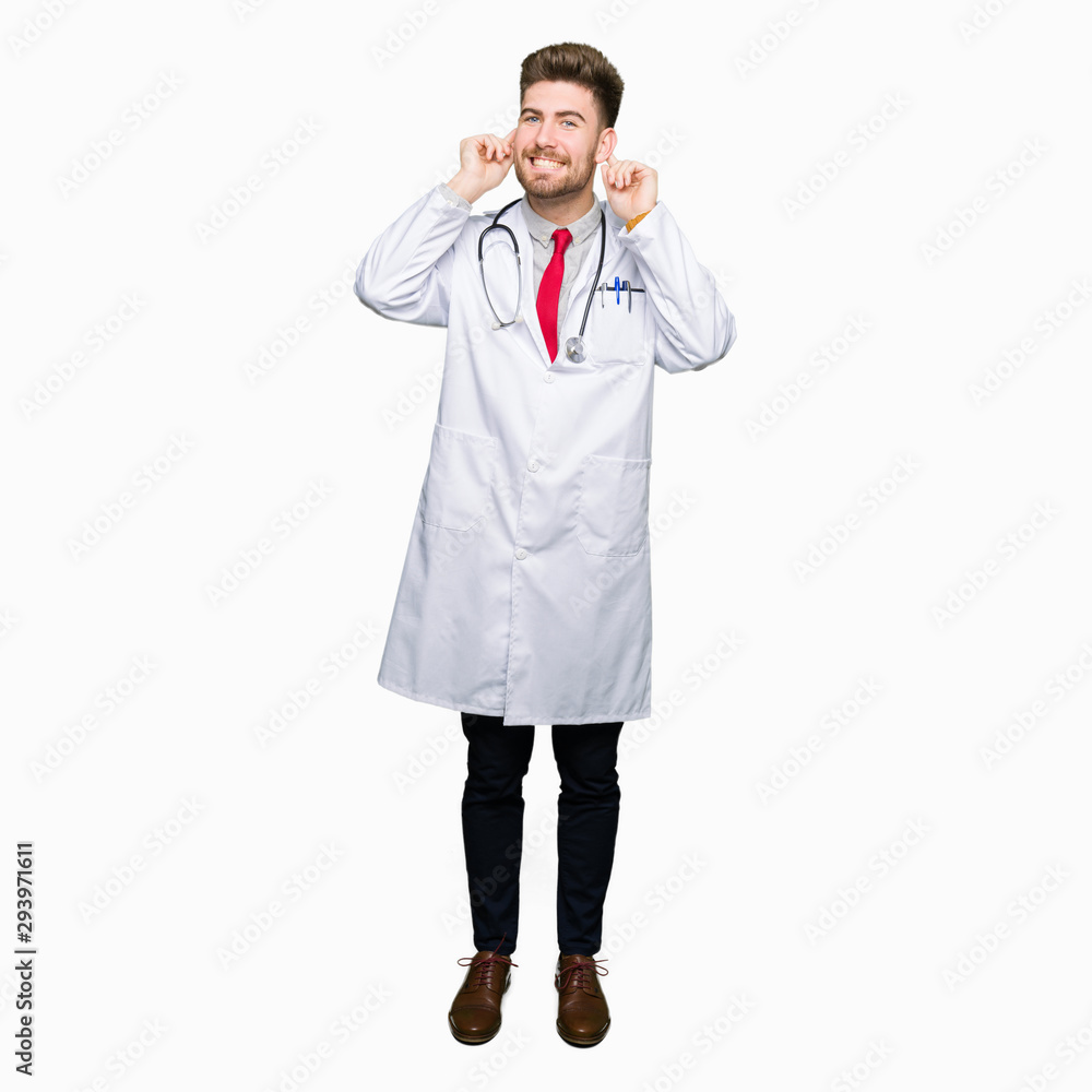 Young handsome doctor man wearing medical coat Smiling pulling ears with fingers, funny gesture. Audition problem Young handsome doctor man wearing medical coat Smiling pulling ears with fingers, funny gesture. Audition problem