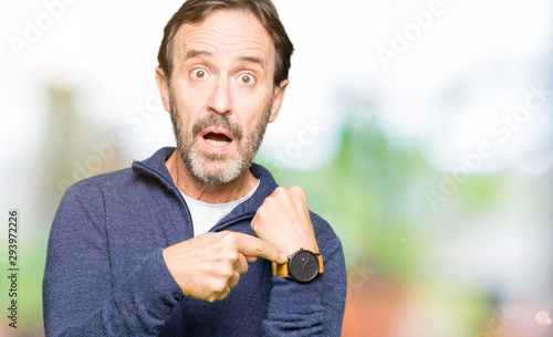 Middle age handsome man wearing a sweater In hurry pointing to watch time, impatience, upset and angry for deadline delay
