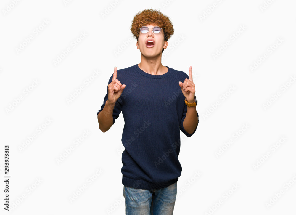 Young handsome man with afro wearing glasses amazed and surprised looking up and pointing with fingers and raised arms. Young handsome man with afro wearing glasses amazed and surprised looking up and pointing with fingers and raised arms.