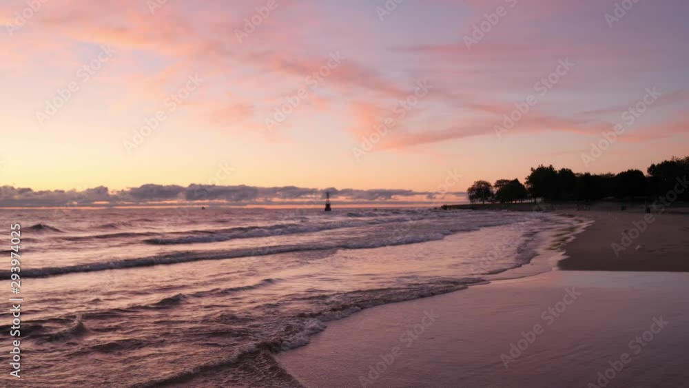 Fantastic sunrise landscape of a sandy beach as waves roll into the shoreline with the sky erupting with pink and purple colors above and reflecting on the lake water below. Fantastic sunrise landscape of a sandy beach as waves roll into the shoreline with the sky erupting with pink and purple colors above and reflecting on the lake water below.