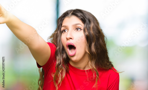 Young beautiful woman wearing casual t-shirt Pointing with finger surprised ahead, open mouth amazed expression, something in front