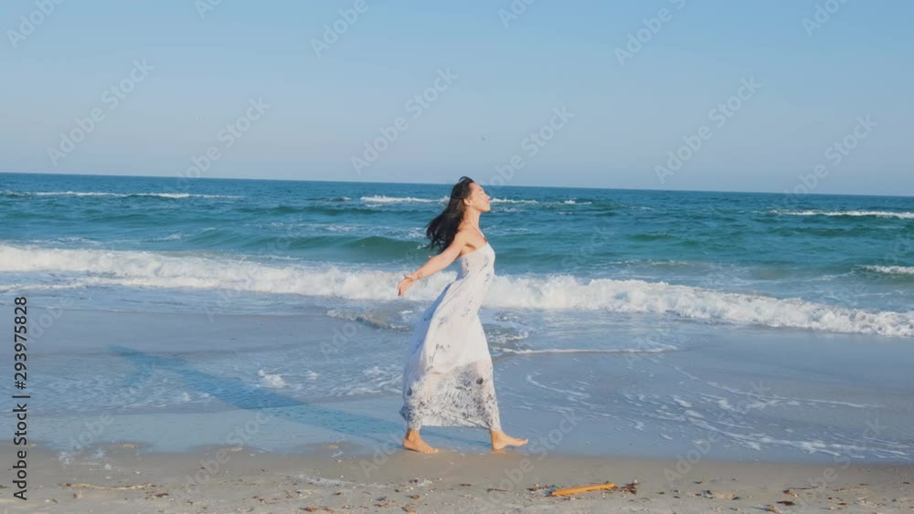 Young beautiful woman dressed in a white dress walk barefoot on the summer beach Young beautiful woman dressed in a white dress walk barefoot on the summer beach