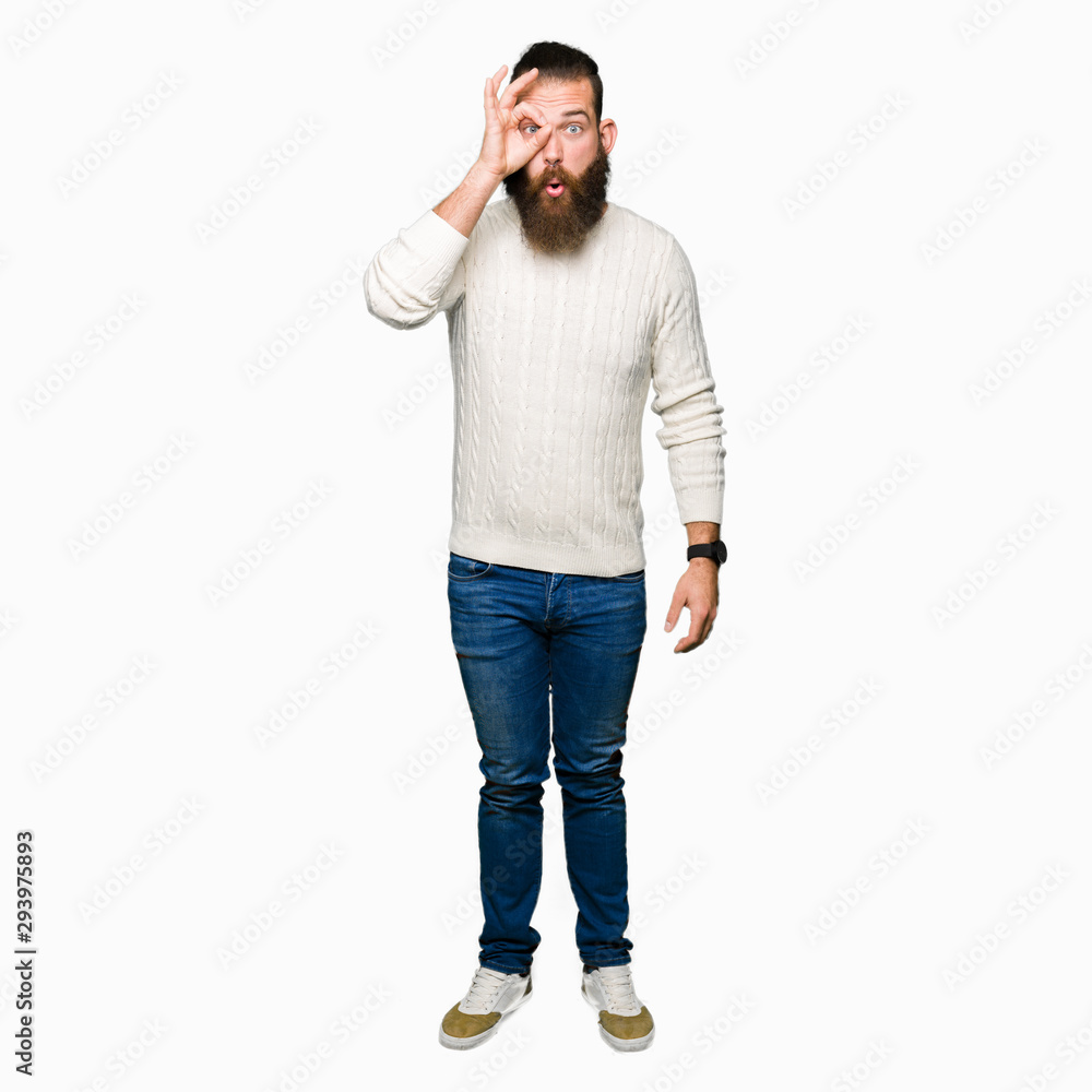 Young hipster man wearing winter sweater doing ok gesture shocked with surprised face, eye looking through fingers. Unbelieving expression. Young hipster man wearing winter sweater doing ok gesture shocked with surprised face, eye looking through fingers. Unbelieving expression.