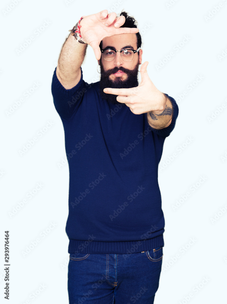Young hipster man with long hair and beard wearing glasses smiling making frame with hands and fingers with happy face. Creativity and photography concept. Young hipster man with long hair and beard wearing glasses smiling making frame with hands and fingers with happy face. Creativity and photography concept.