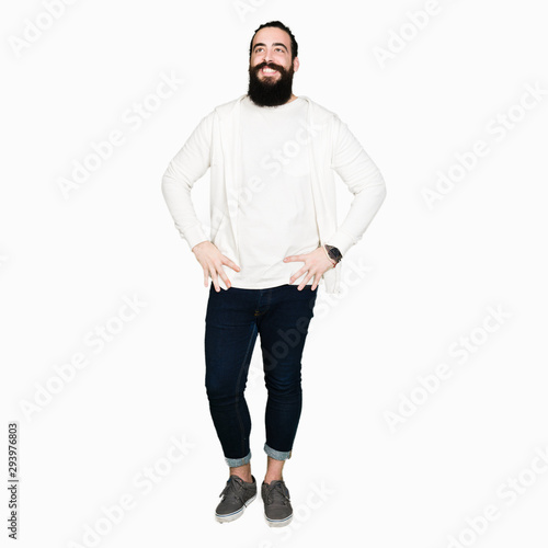 Young man with long hair and beard wearing sporty sweatshirt looking away to side with smile on face, natural expression. Laughing confident.