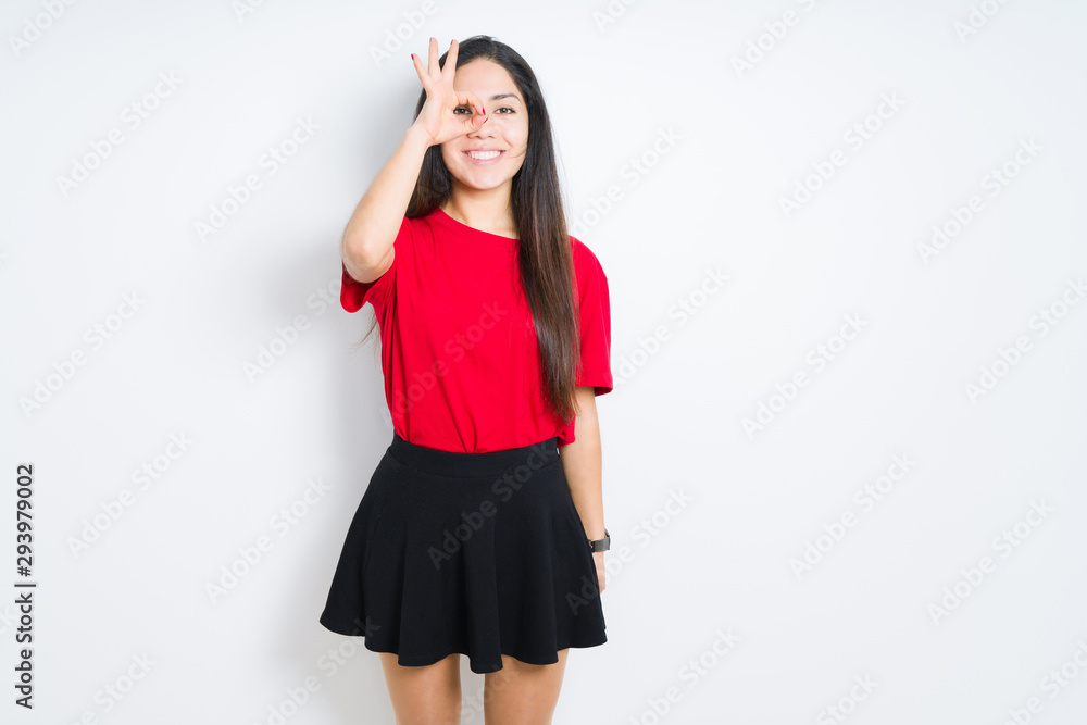 Beautiful brunette woman wearing red t-shirt and skirt over isolated background doing ok gesture with hand smiling, eye looking through fingers with happy face. Beautiful brunette woman wearing red t-shirt and skirt over isolated background doing ok gesture with hand smiling, eye looking through fingers with happy face.