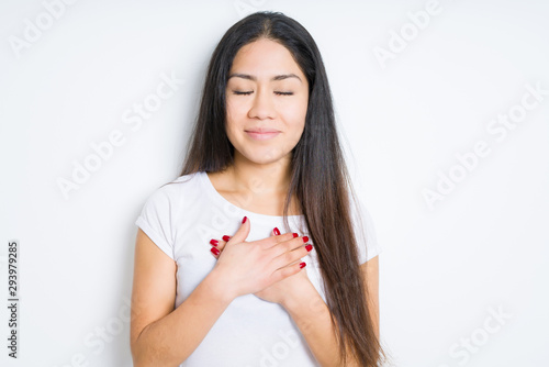 Beautiful brunette woman over isolated background smiling with hands on chest with closed eyes and grateful gesture on face. Health concept.