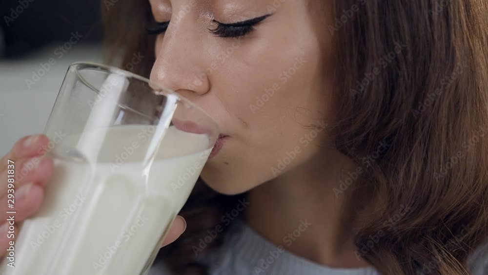 Lovely joyful satisfied woman drinking a glass of milk and posing on camera with sincerely smile Lovely joyful satisfied woman drinking a glass of milk and posing on camera with sincerely smile