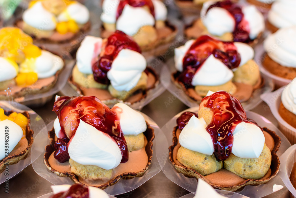 Fototapeta premium Close up of profiteroles, cream puffs or chou à la crème with whipped cream and strawberry jam, in displayed for sale at an weekend street market, selective focus