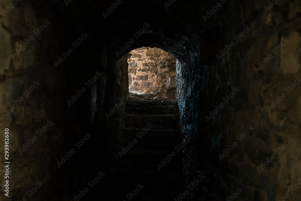 twilight darkness lighting in medieval castle underground cage narrow passage between cold stone walls with exit light view 