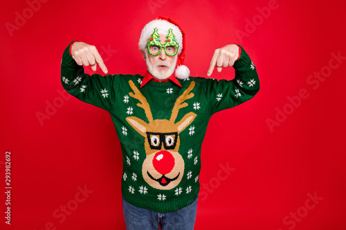 Photo of santa looking on low x-mas shopping prices indicate fingers on cheap jumper wear x-mas tree shape specs ugly ornament sweater isolated red background photo