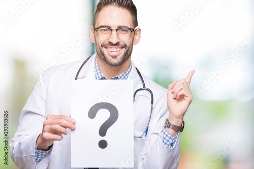 Handsome young doctor man holding paper with question mark over isolated background very happy pointing with hand and finger to the side