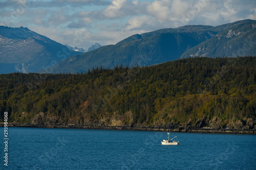 A small fishing ship sailing in the ocean on the background of mountains and green forest
