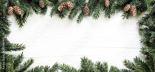 Christmas frame of fir branches and pine cones on white wooden board