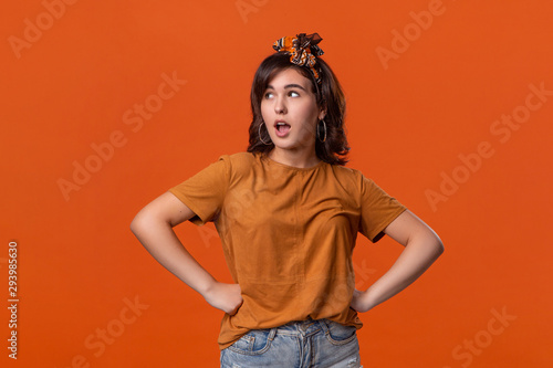 Pretty brunette woman in a t-shirt and beautiful headband expressing emotion of surprise standing isolated over orange background. © ianachyrva