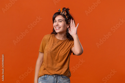 Canvastavla Pretty brunette woman in a t-shirt and beautiful headband holding hand close to ear listening to secret information