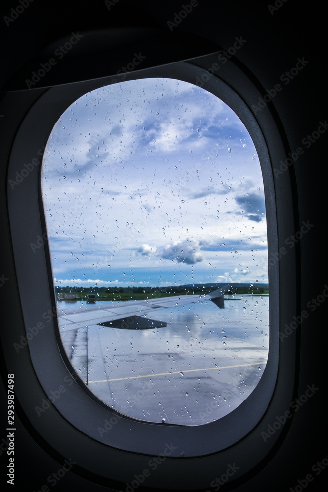 Airplane window covered with rain drops. And the view of the airplane right wing and outdoor at the airport runway. Selective focus. Copy space. Airplane window covered with rain drops. And the view of the airplane right wing and outdoor at the airport runway. Selective focus. Copy space.