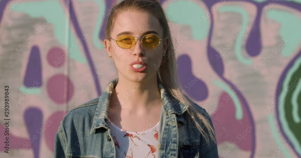Portrait of Young Blonde Woman Blowing Gum in Hippy Shades. Festival Girl Student in Pink Bubble Graffiti Art Setting. Cool Teen Boho in Vintage Denim Jacket. A City Fashion Summer Tourist. Portrait of Young Blonde Woman Blowing Gum in Hippy Shades. Festival Girl Student in Pink Bubble Graffiti Art Setting. Cool Teen Boho in Vintage Denim Jacket. A City Fashion Summer Tourist.