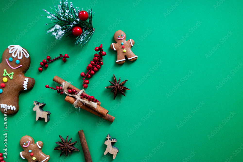Gingerbread men, cinnamon, anise, mistletoe and deers ornaments on green background. Flat lay and copy space. Christmas concept.