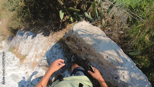 POV man walking down the stone stair path to amazing bay on Ponza Island coast cliff taking pictures with smartphone. Action camera on head.