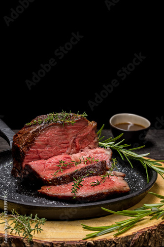 Sous-vide grilled beef steak with herbs in cast-iron skillet on wooden plate.