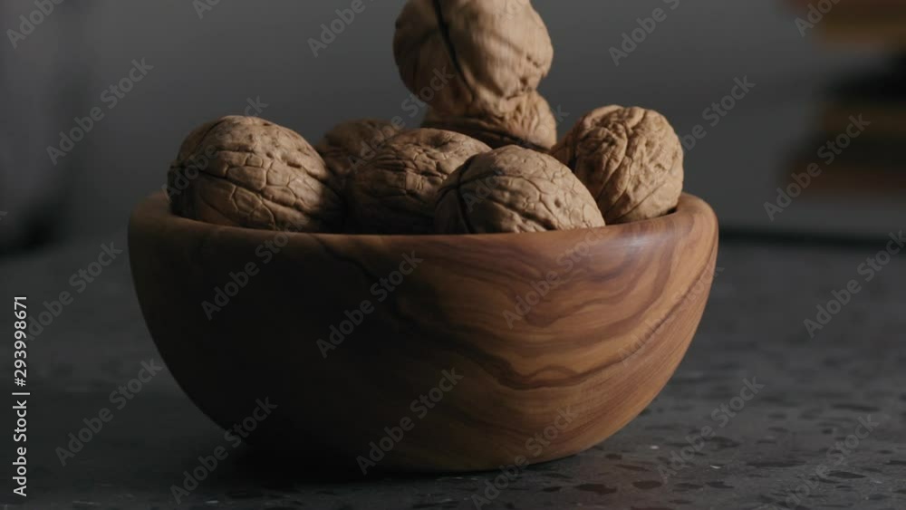 Slow motion shelled walnuts falling into wooden bowl on terrazzo countertop Slow motion shelled walnuts falling into wooden bowl on terrazzo countertop