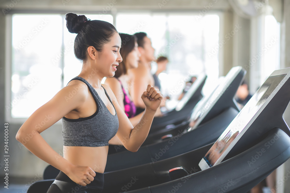 Beautiful Asian women Thai people have tan skin, long hair and tied hair in a sports bra doing exercise by running on the electric treadmill in the fitness room in Thailand. - obrazy, fototapety, plakaty 