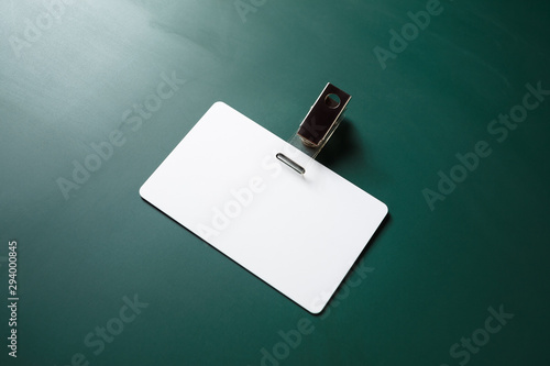 Blank white plastic badge on green chalkboard background. Empty ID card. Space for text. Template for branding identity.