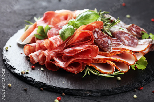 Marble cutting board with prosciutto, bacon, salami and sausages on wooden background. Rustic Meat platter
