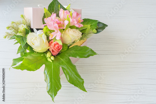 Beautiful bouquet of bright flowers in basket on white wooden background. 