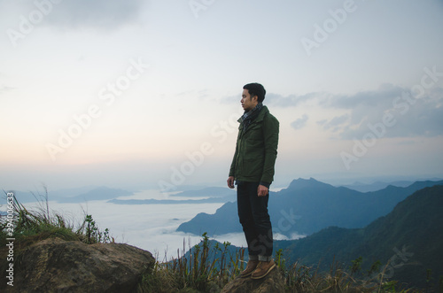 young man standing on hill is wearing green coat