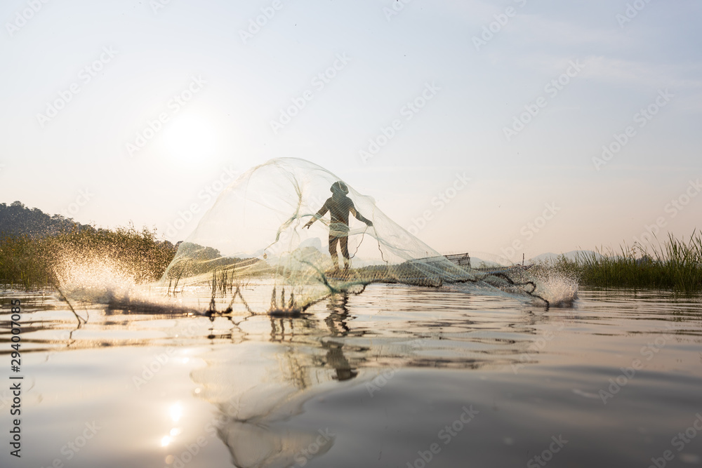 Asian fishermen throwing fishing net during sunset on wooden boat at the lake. Concept Fisherman's Lifestyle in countryside. Lopburi, Thailand, Asia