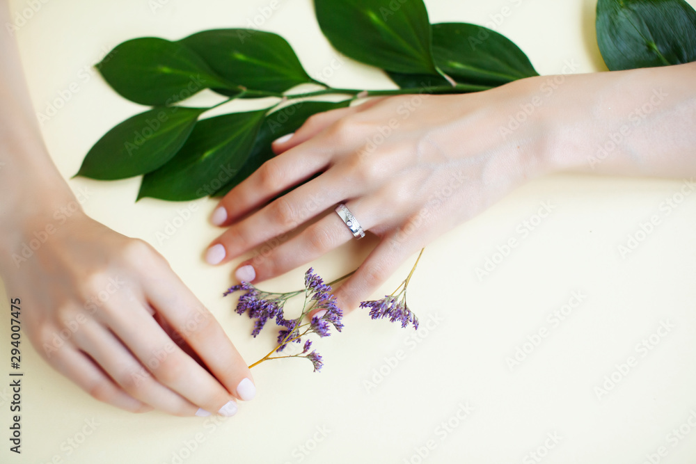 Fototapeta premium pretty perfect woman hands with white manicure and little flowers on colorful green background, spa concept closeup