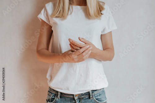 Blond hair woman posing near a light wall. Beautiful young caucasian girl. Hand gestures. Emotion. Casual clothing. Studio model in work. Strong woman, future is female. Jeans and white blank t-shirt