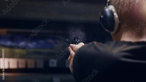 Shooting gallery. A young man preparing the gun and shooting with a firearms. A smoking gun. A concentrated young man shooting on a shooting range. Spark. Bullet. Shot.